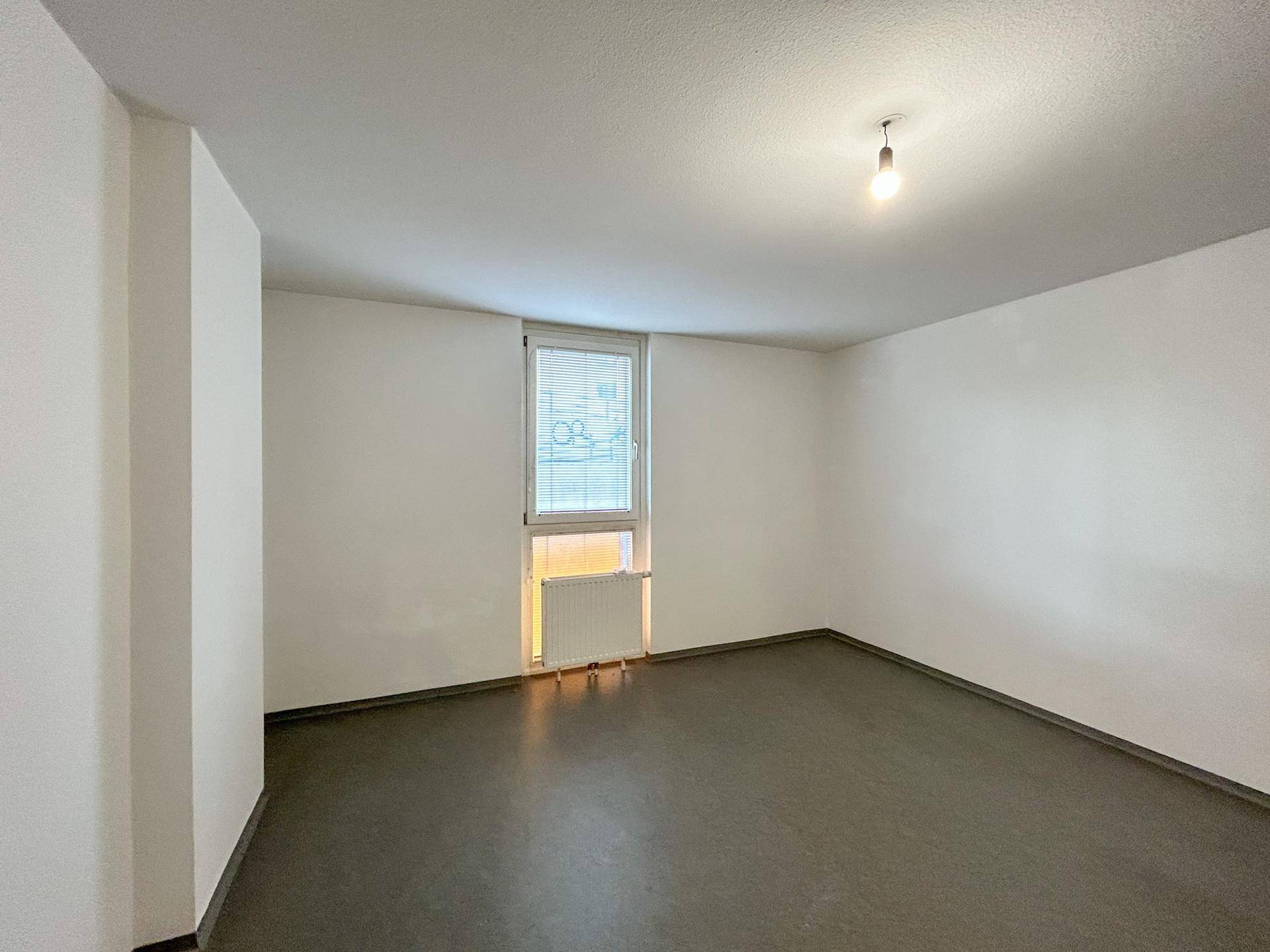 Unmöbliertes Schlafzimmer mit einem Fenster, Heizkörper und dunklem, pflegeleichtem Bodenbelag.