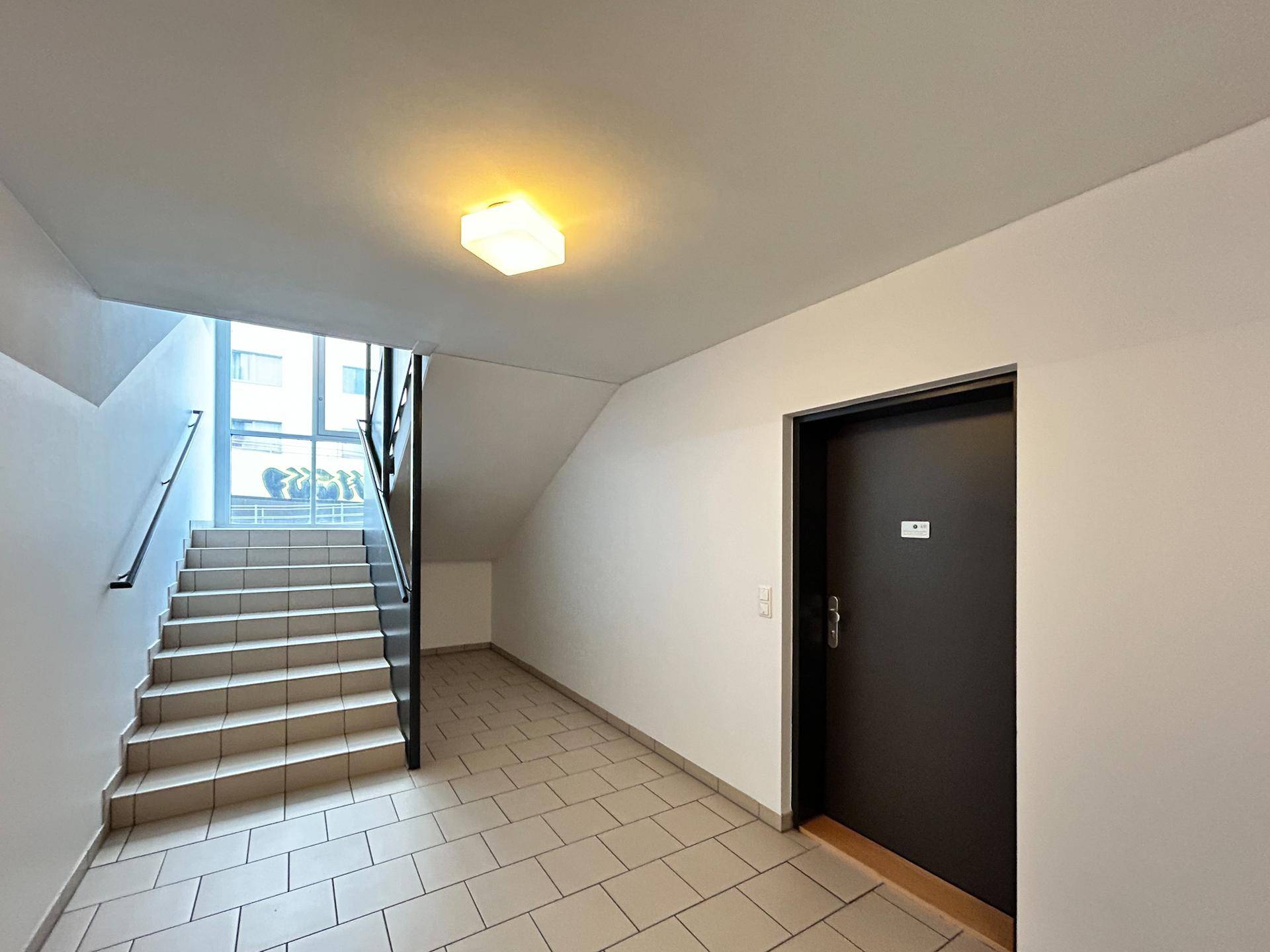 Helles Treppenhaus mit Fliesenboden, modernem Geländer und einer Wohnungstür im Mehrfamilienhaus.