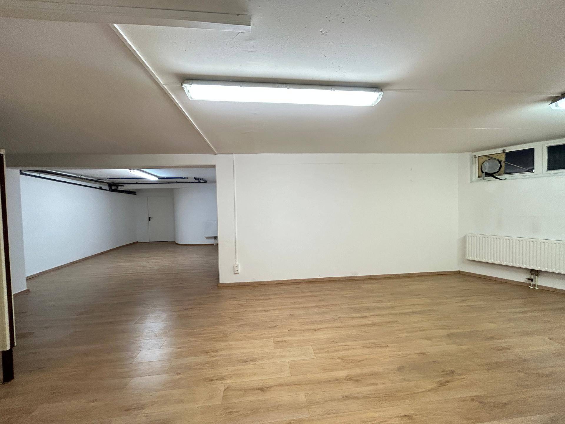 Heller Lagerraum mit Laminatboden und weißen Wänden, ausgestattet mit Heizung und Deckenbeleuchtung.