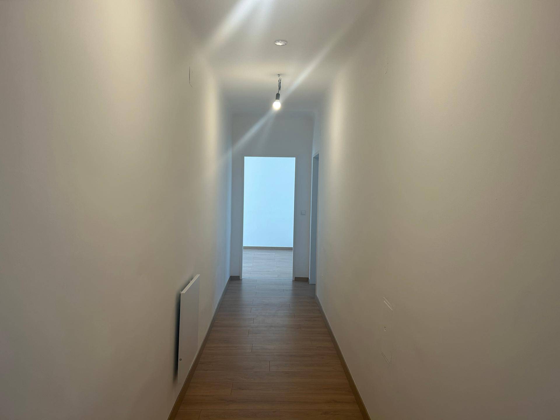 Langer, heller Flur mit Holzfußboden und weiß gestrichenen Wänden, der zu weiteren Räumen führt.