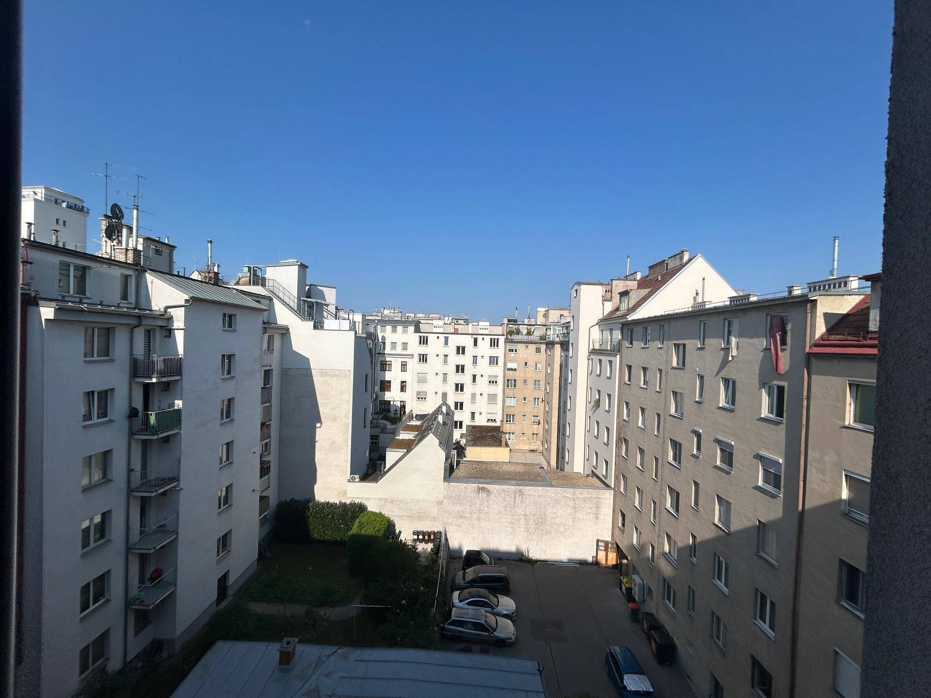 Weitläufiger Blick über die Dächer und Innenhöfe einer städtischen Wohngegend unter blauem Himmel.