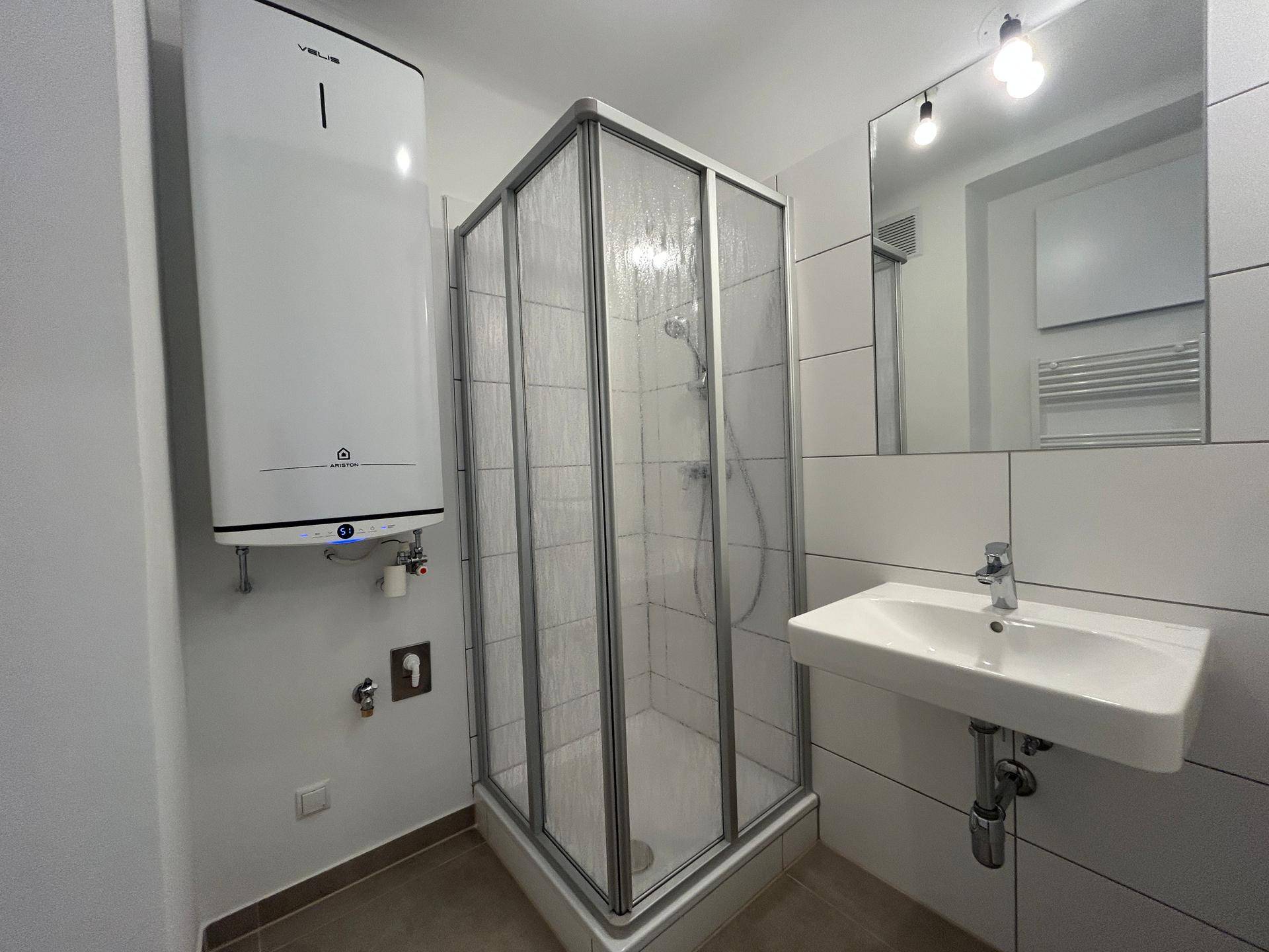 Modernes Badezimmer mit Duschkabine, Waschbecken und einem Warmwasserboiler an der Wand.