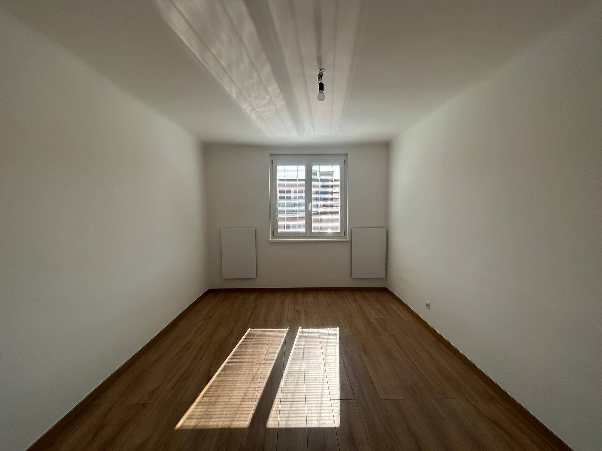 Helles Schlafzimmer mit Holzfußboden, weißen Wänden und einem großen Fenster, das viel Licht hereinlässt.