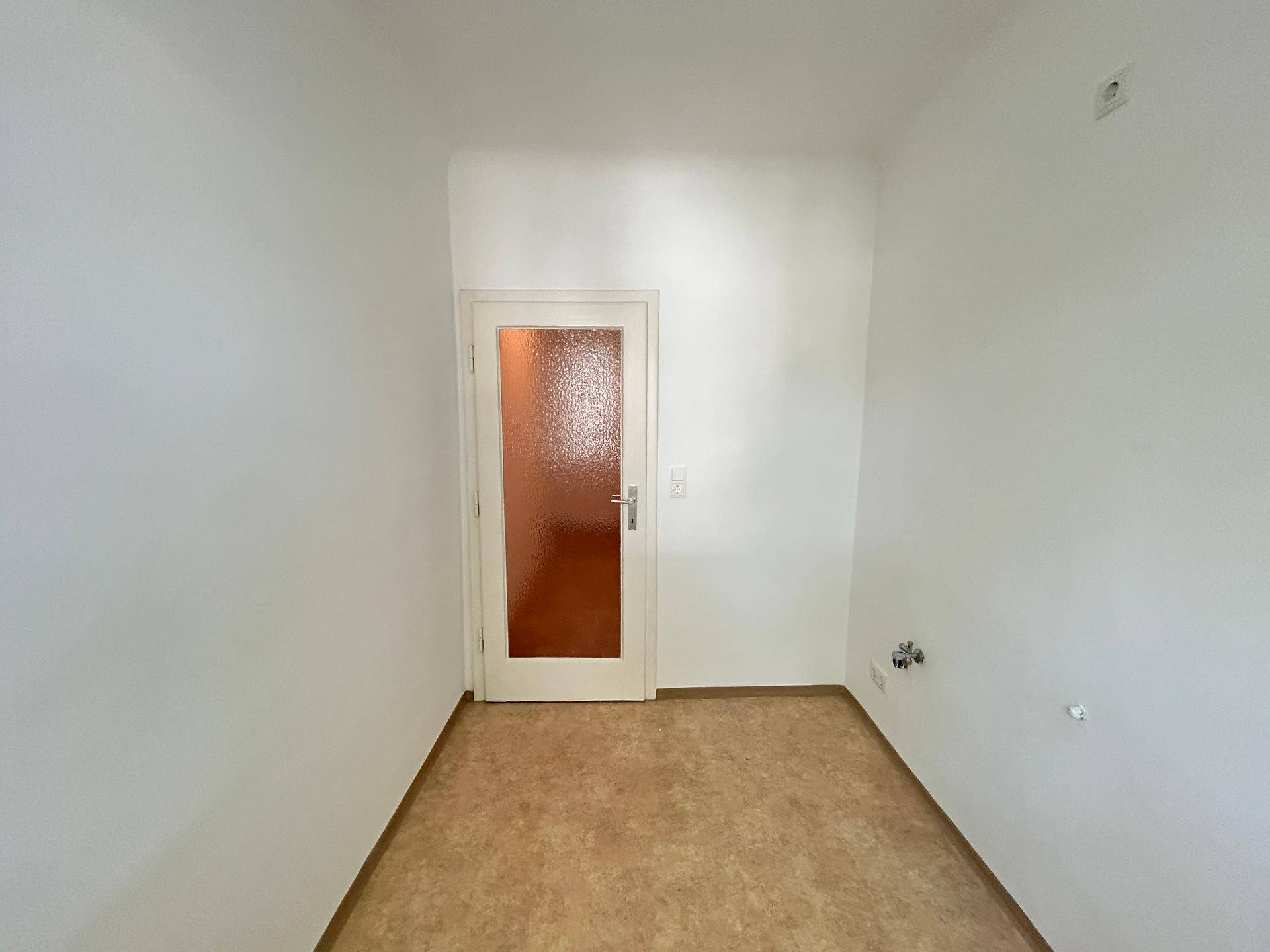 Kleiner Raum mit Tür und Anschlüssen an der Wand, geeignet als Abstellraum oder kleine Küche.