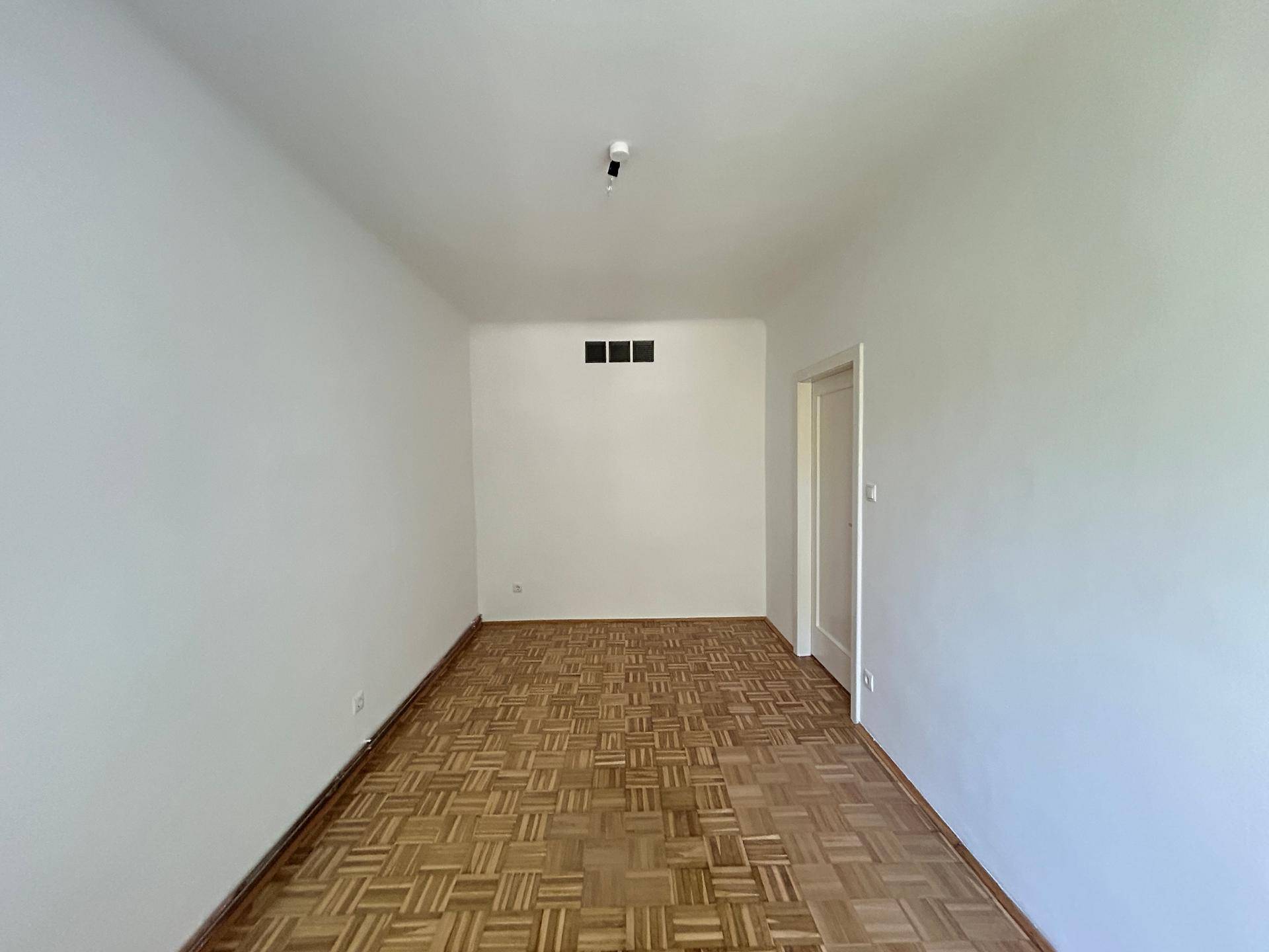 Wohnzimmer mit Parkettboden und Belüftungselementen an der Wand, in gutem Zustand.