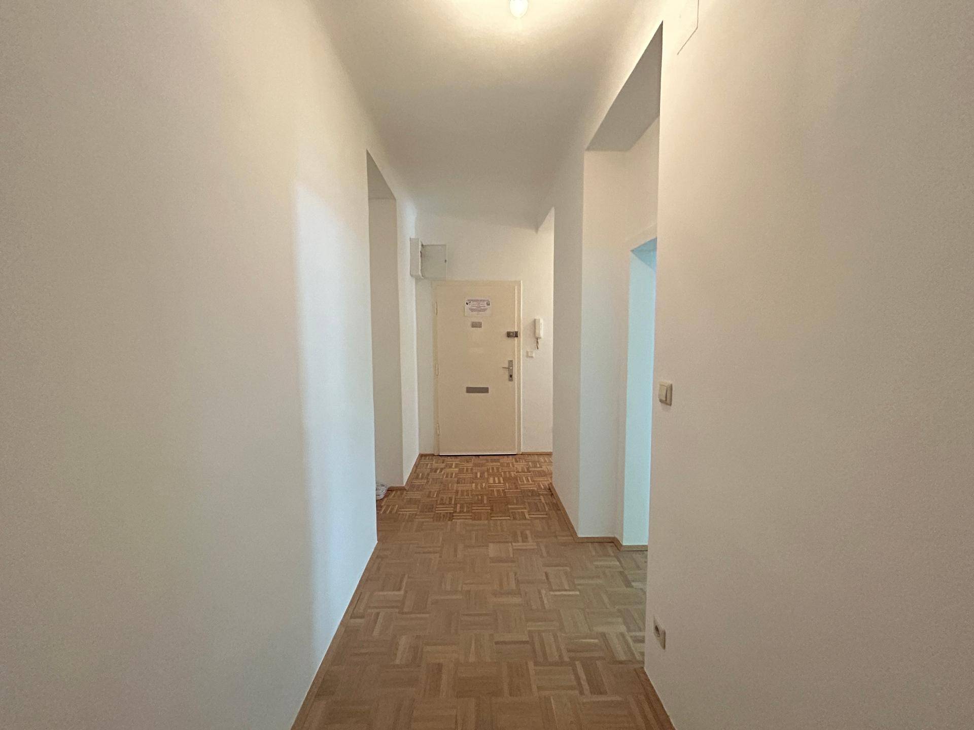 Heller Flur mit klassischem Parkettboden und weiß gestrichenen Wänden, der zu weiteren Räumen führt.