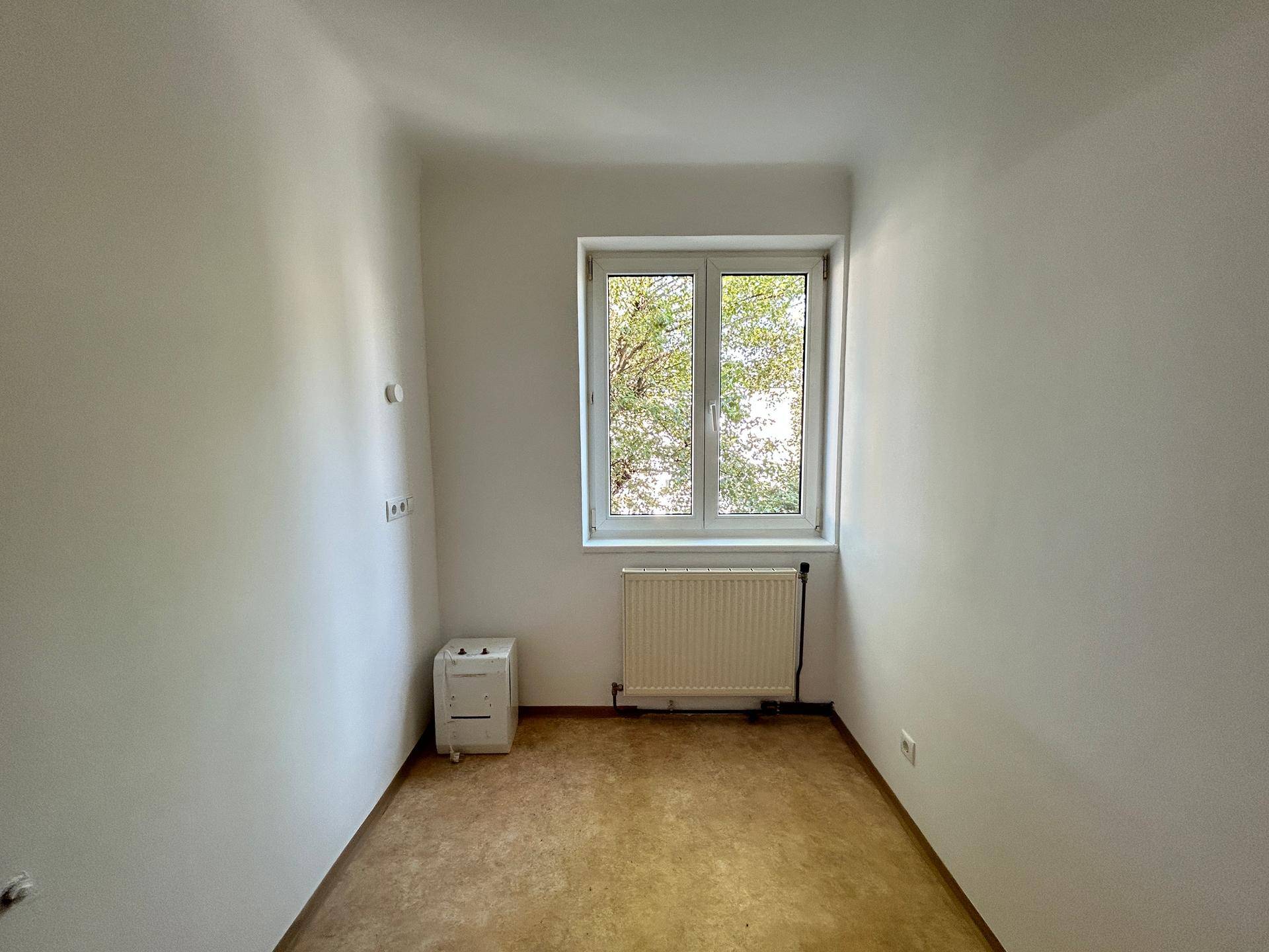 Kleiner Raum mit Fenster, Heizkörper und hellem Bodenbelag, möglicherweise ein Kabinett oder Abstellraum.