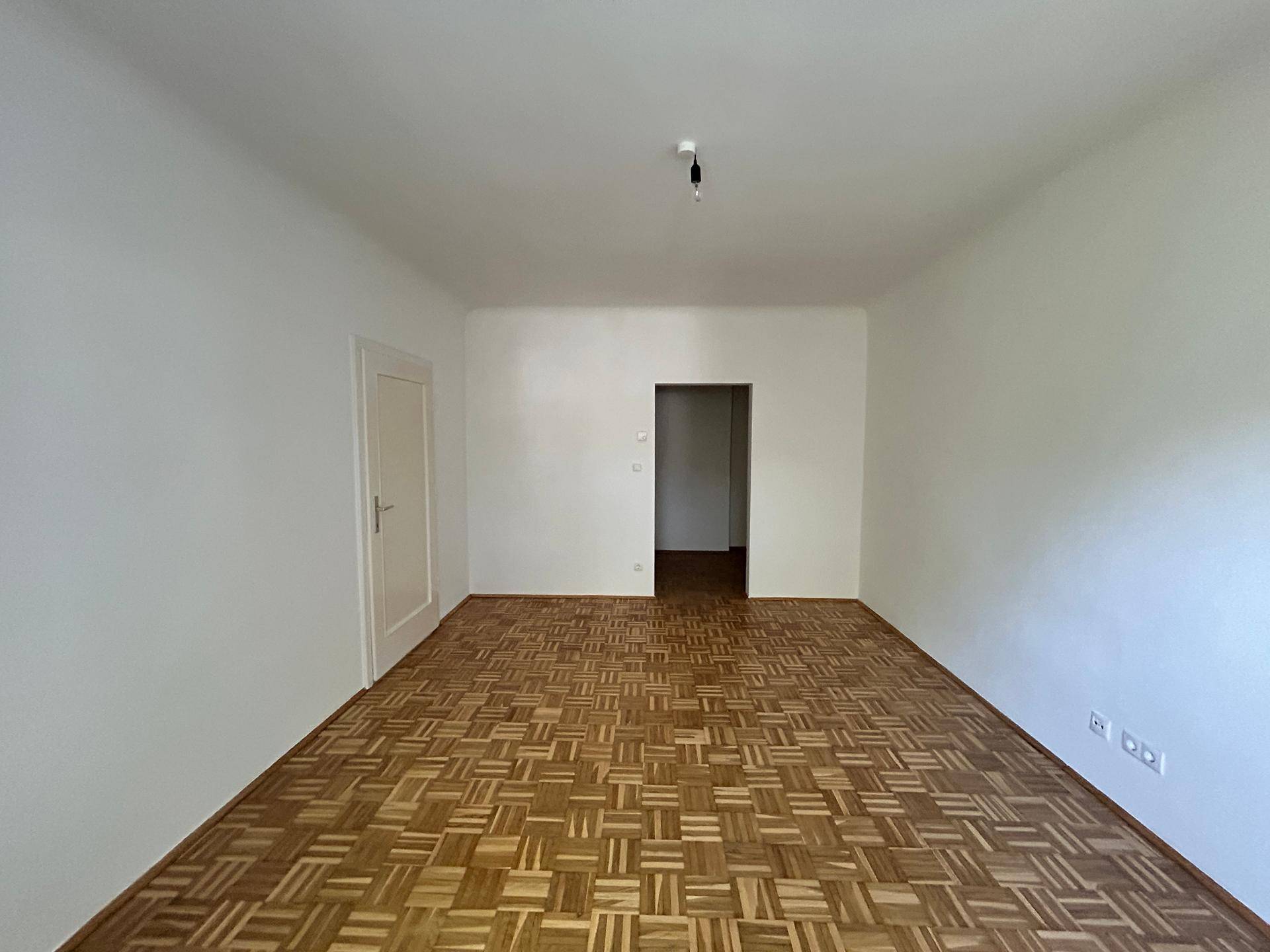 Helles Wohnzimmer mit Parkettboden und Zugang zu weiteren Räumen der Wohnung.