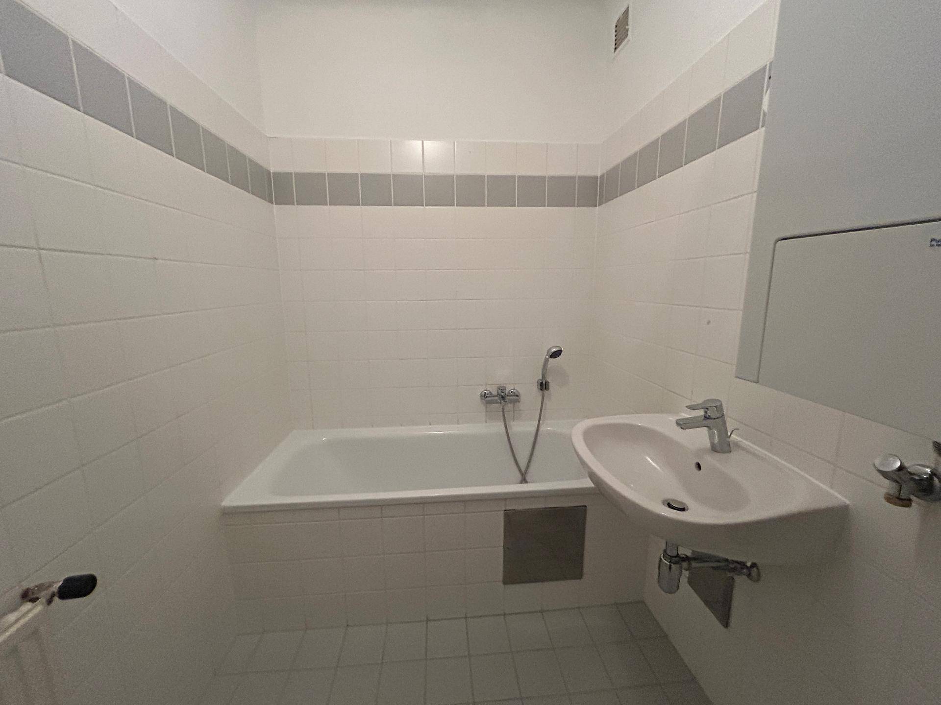 Gefliestes Badezimmer mit Badewanne und Waschbecken, in einem funktionalen Zustand mit grauen Akzenten.