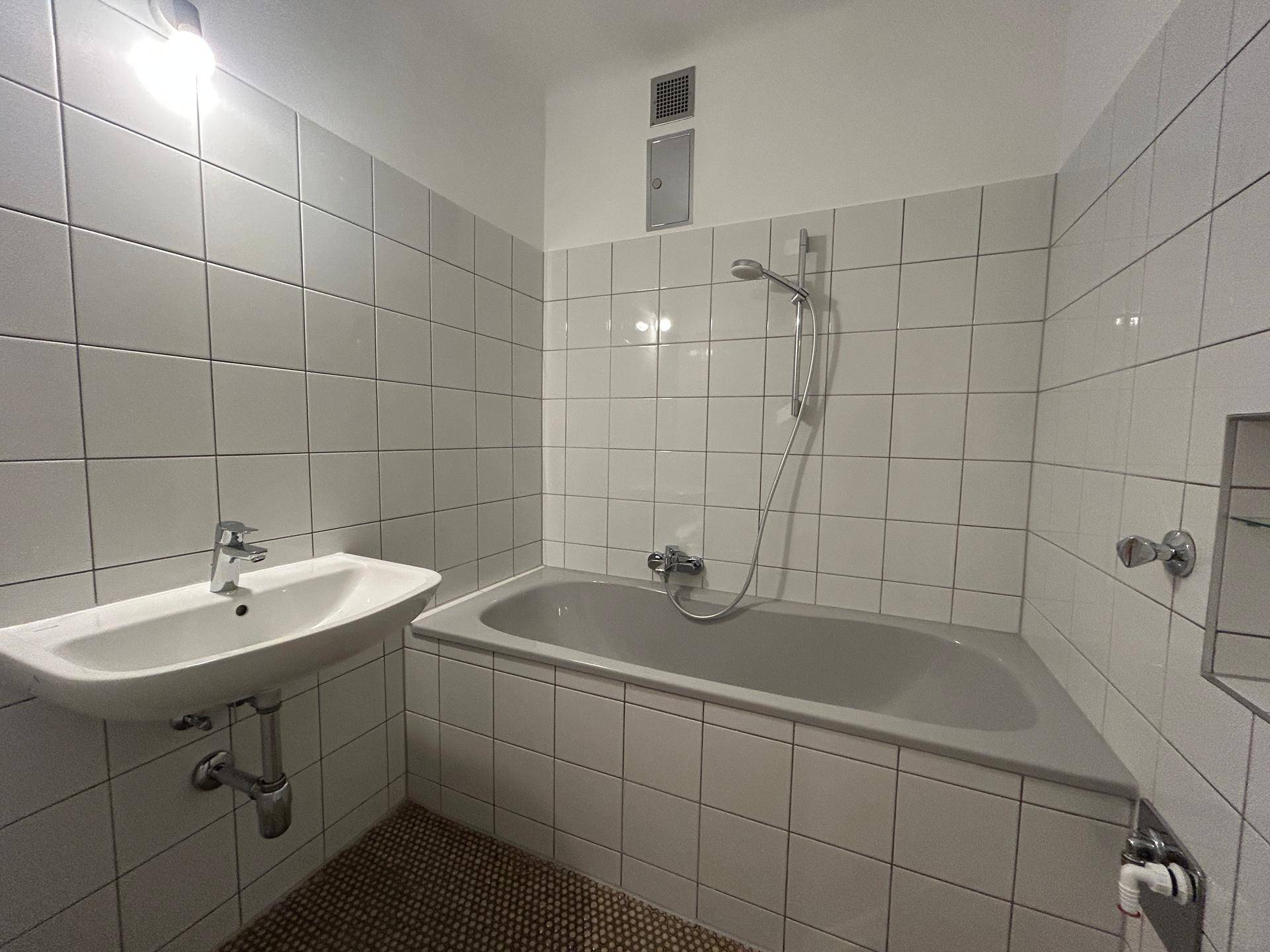 Badezimmer mit Badewanne, Waschbecken und weißen Fliesen, in einem funktionalen Zustand.