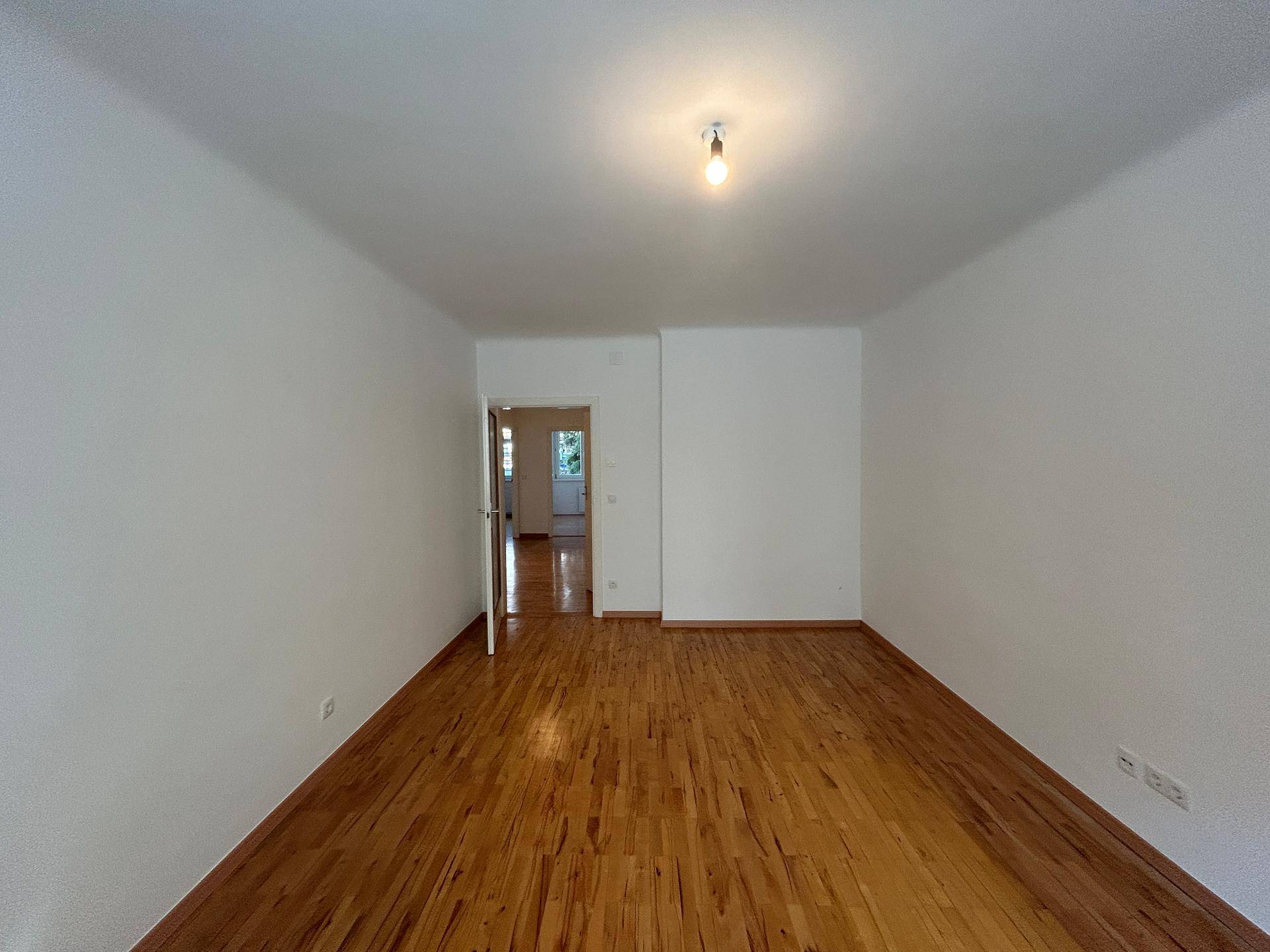 Geräumiger, heller Raum mit Holzboden und weißen Wänden, ideal als Wohnzimmer nutzbar.