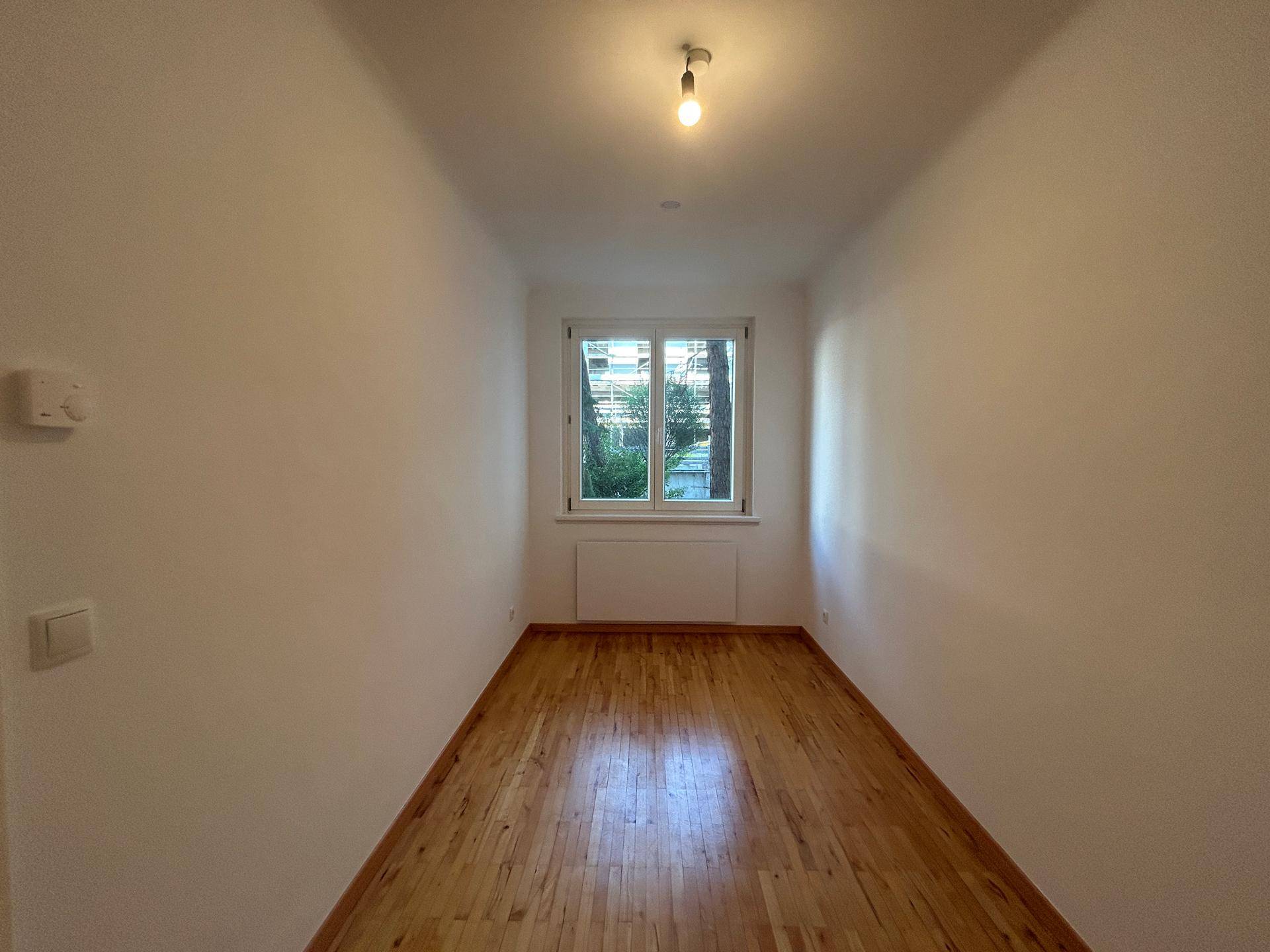 Helles Zimmer mit Holzboden und Fenster, das sich gut als Schlafzimmer oder Büro eignet.