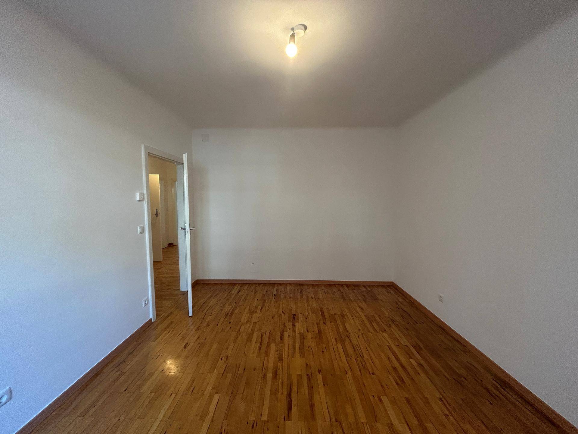 Geräumiger, heller Raum mit Holzboden und weißen Wänden, der vielseitig nutzbar ist.