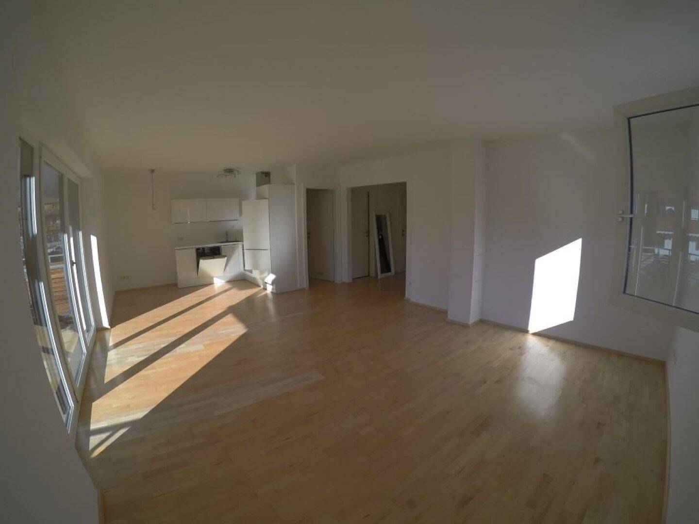 Heller Wohnbereich mit Holzboden und großen Fenstern, die viel Sonnenlicht hereinlassen.