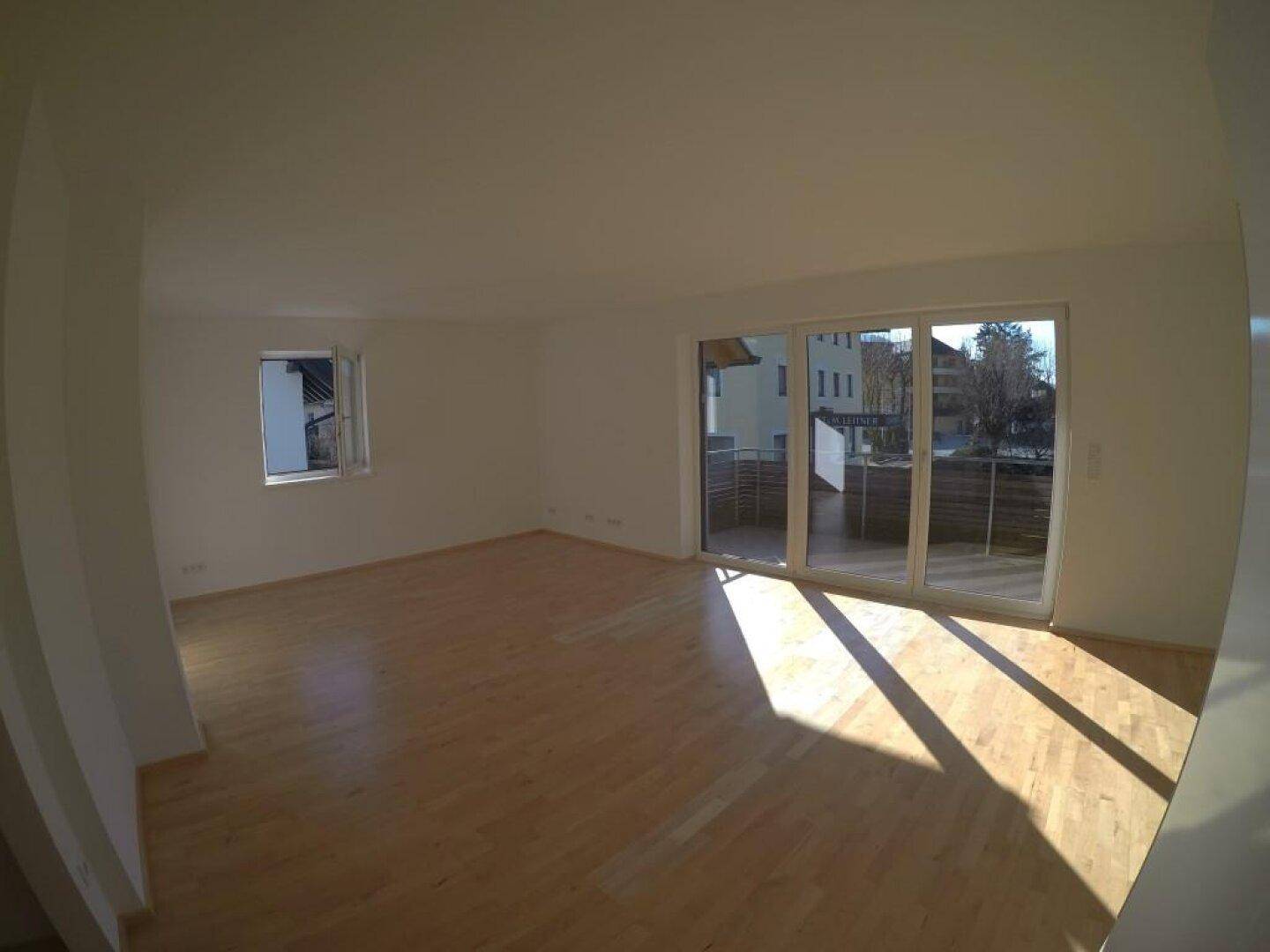Geräumiger Wohnbereich mit Holzboden und Zugang zu einem Balkon oder einer Terrasse.