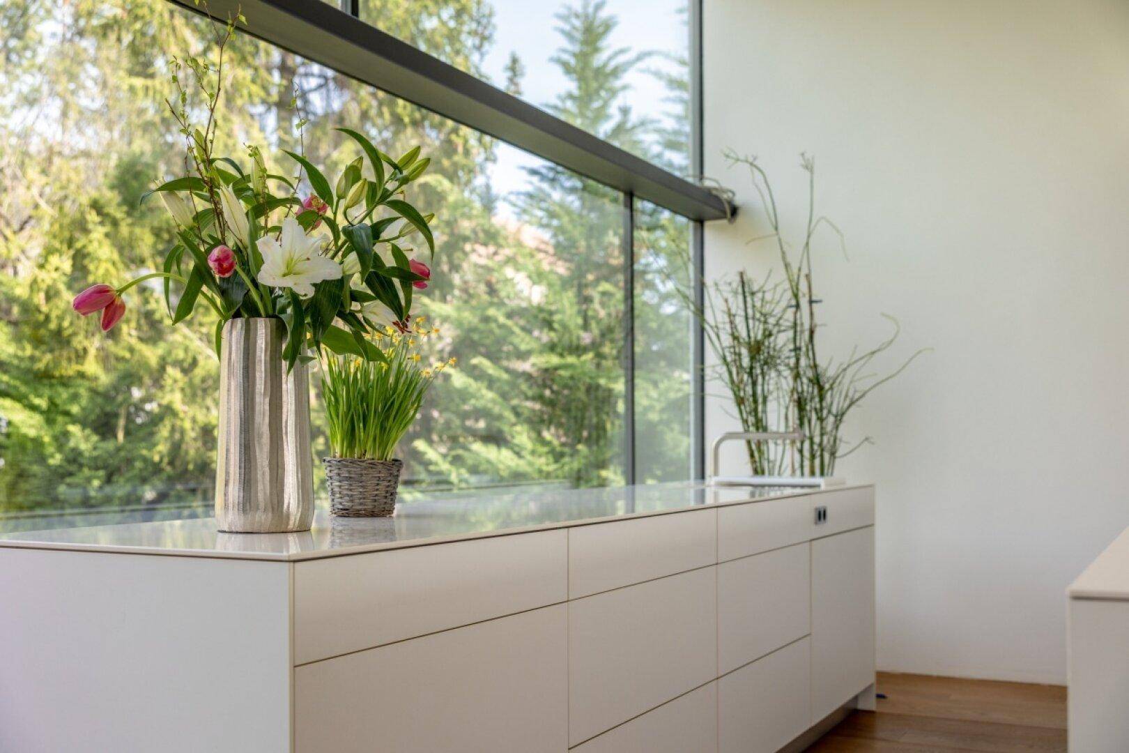 Helle Küchenzeile mit frischen Blumen und großem Fenster mit Blick ins Grüne.
