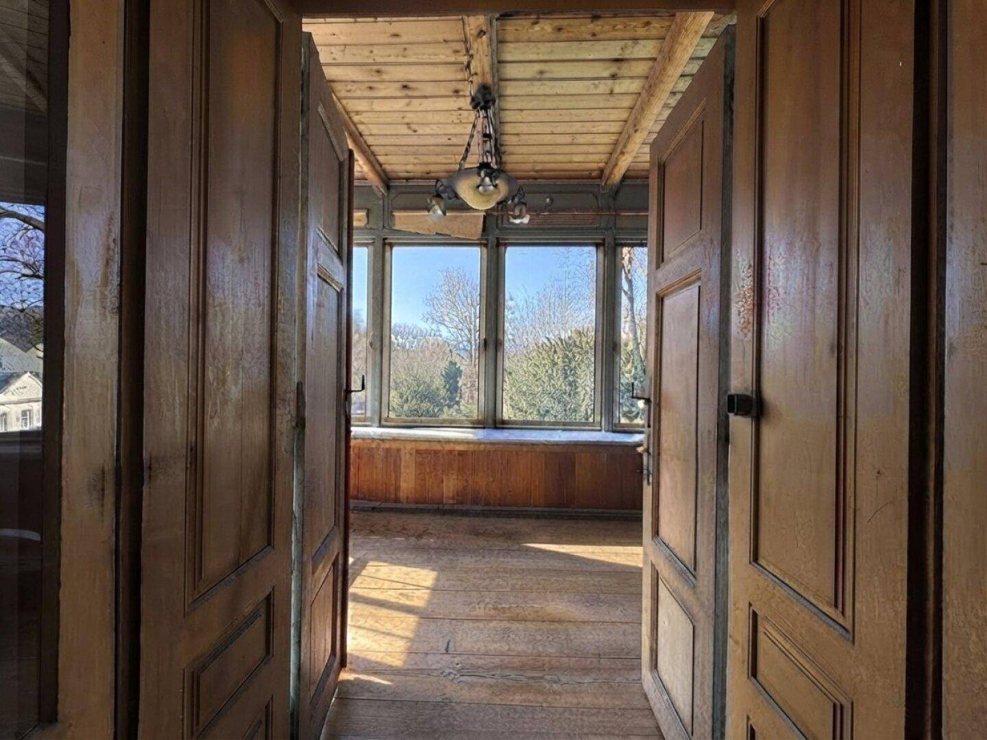 Heller Wintergarten mit Holzboden und großen Fenstern, die viel Tageslicht hereinlassen.