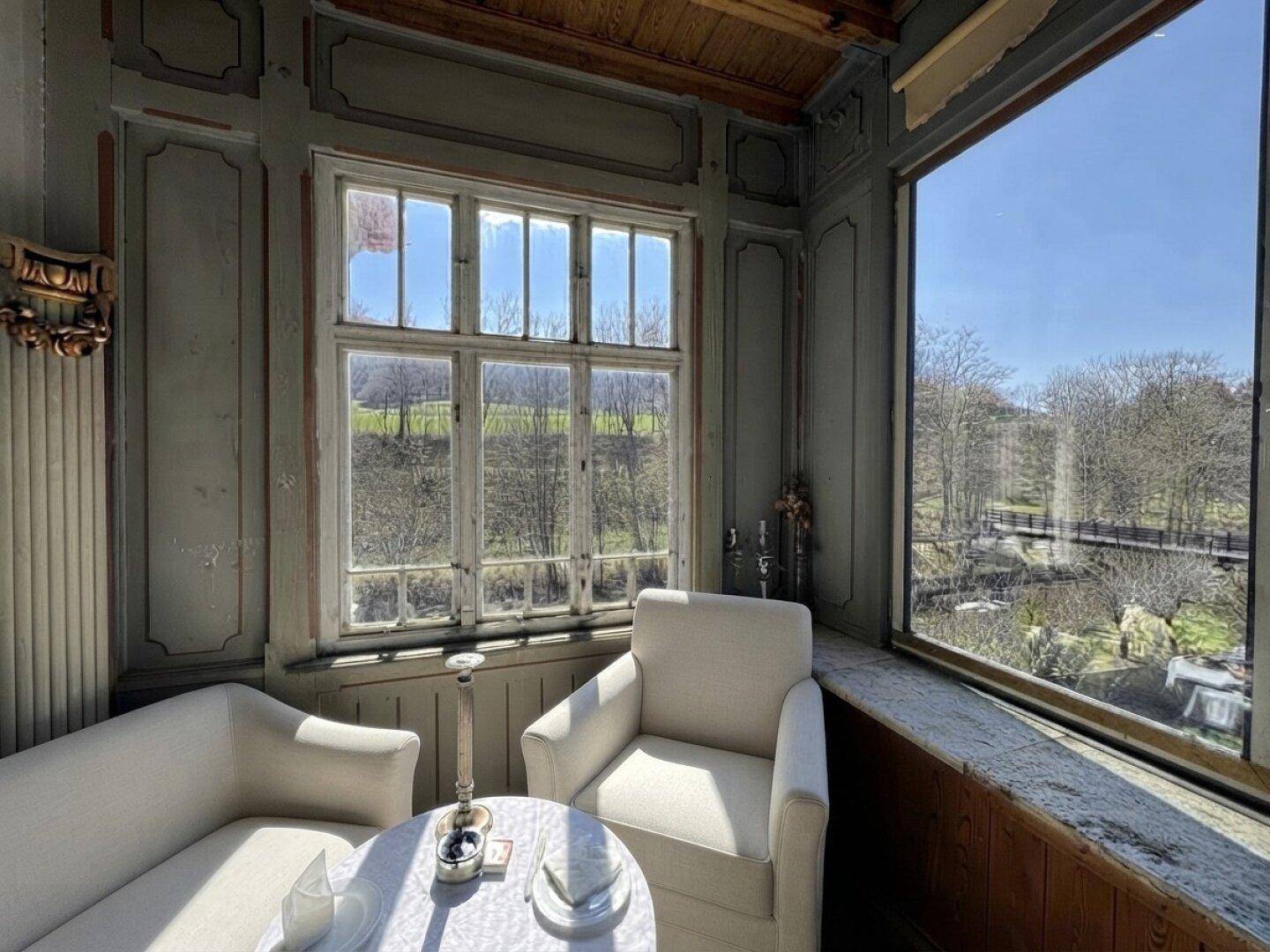 Gemütlicher Wintergarten mit Sitzgelegenheiten und weitem Blick auf die grüne Umgebung.