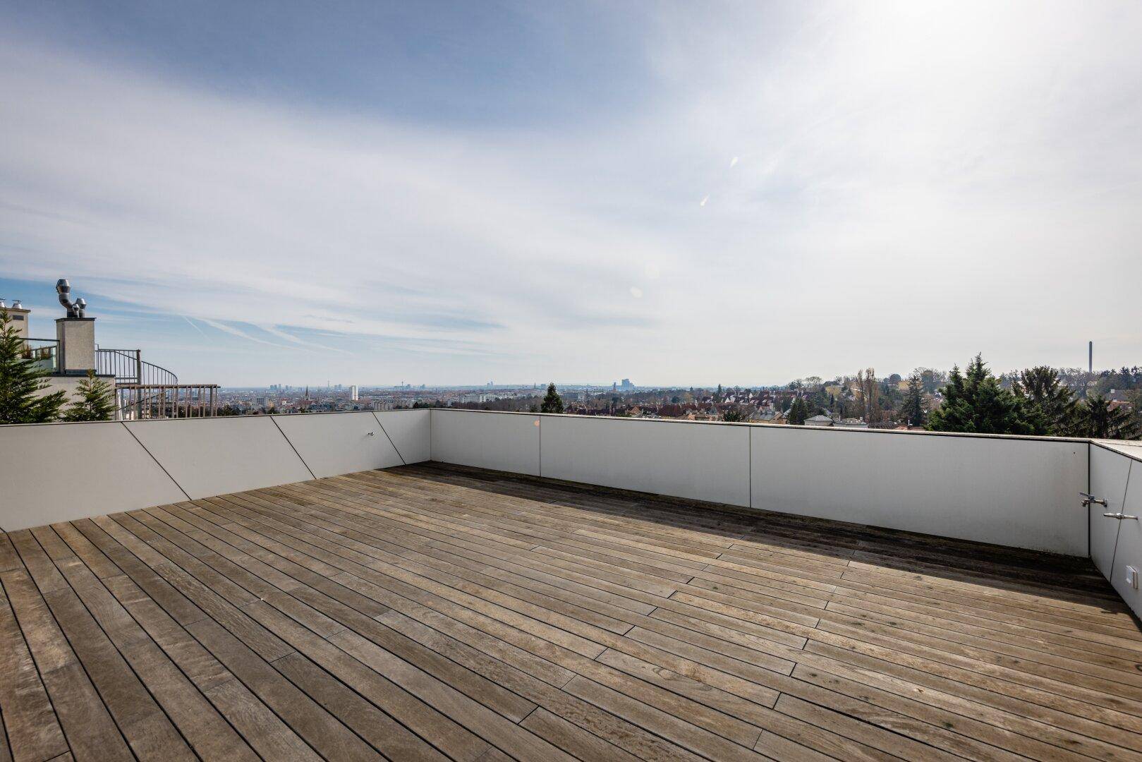Große Dachterrasse mit Holzboden und weitem Blick über die Stadt unter blauem Himmel.