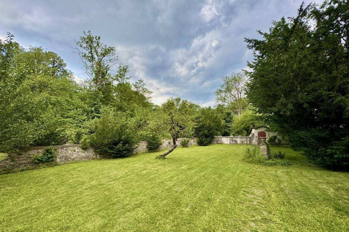 Weitläufiger Gartenbereich mit gepflegtem Rasen, umgeben von Bäumen und einer Steinmauer.