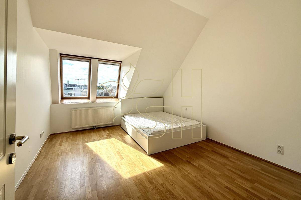 Helles Schlafzimmer mit Bett, Holzparkettboden und großen Fenstern unter der Dachschräge.