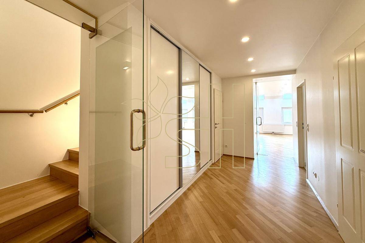 Langer Flur mit Einbauschränken, Holzparkett und einer Treppe, die in die obere Etage führt.