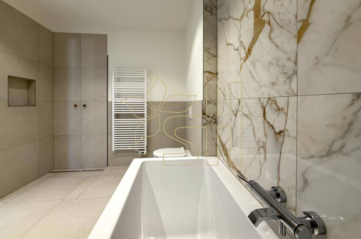 Modernes Badezimmer mit Badewanne, eleganten Marmorfliesen und einem praktischen Handtuchheizkörper.