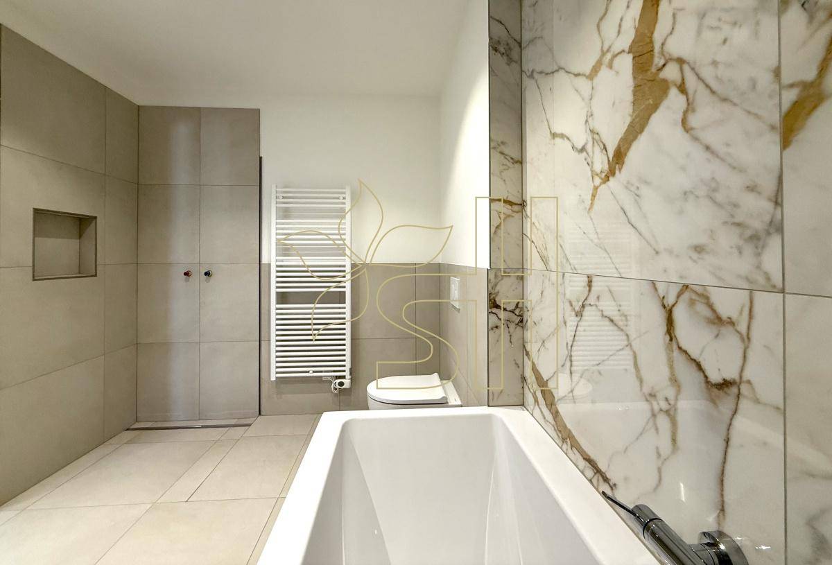 Modernes Badezimmer mit Badewanne, eleganten Marmorfliesen und einem praktischen beheizten Handtuchhalter.