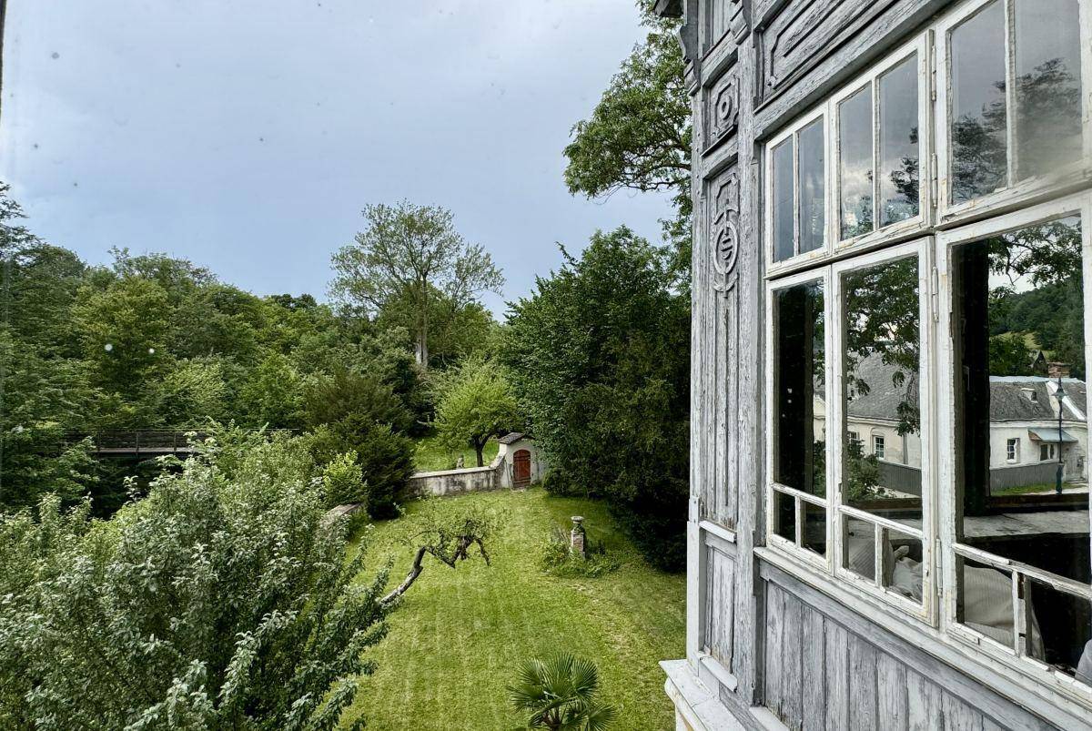 Blick aus einem historischen Fenster auf den weitläufigen Garten und die umliegende grüne Landschaft.
