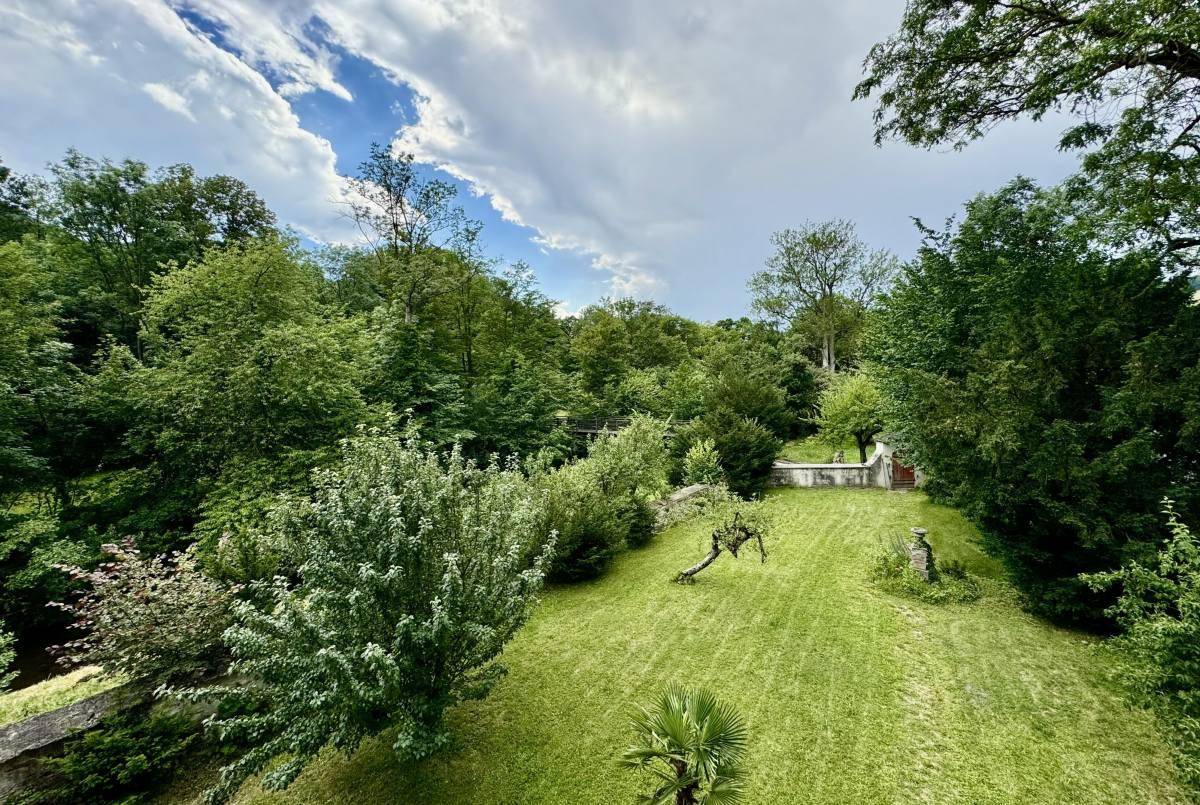 Panoramablick auf den weitläufigen Garten mit Rasenflächen und altem Baumbestand unter blauem Himmel.