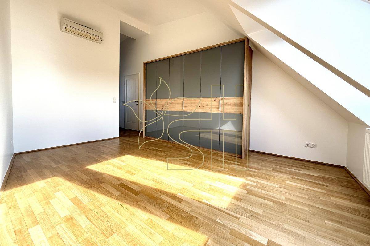 Schlafzimmer mit großem Einbauschrank, Holzparkett, Dachschräge und Klimaanlage.