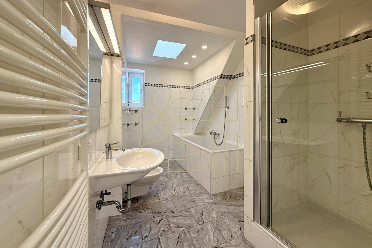 Badezimmer mit Badewanne, Duschkabine, Waschbecken, Dachfenster und beheiztem Handtuchhalter.