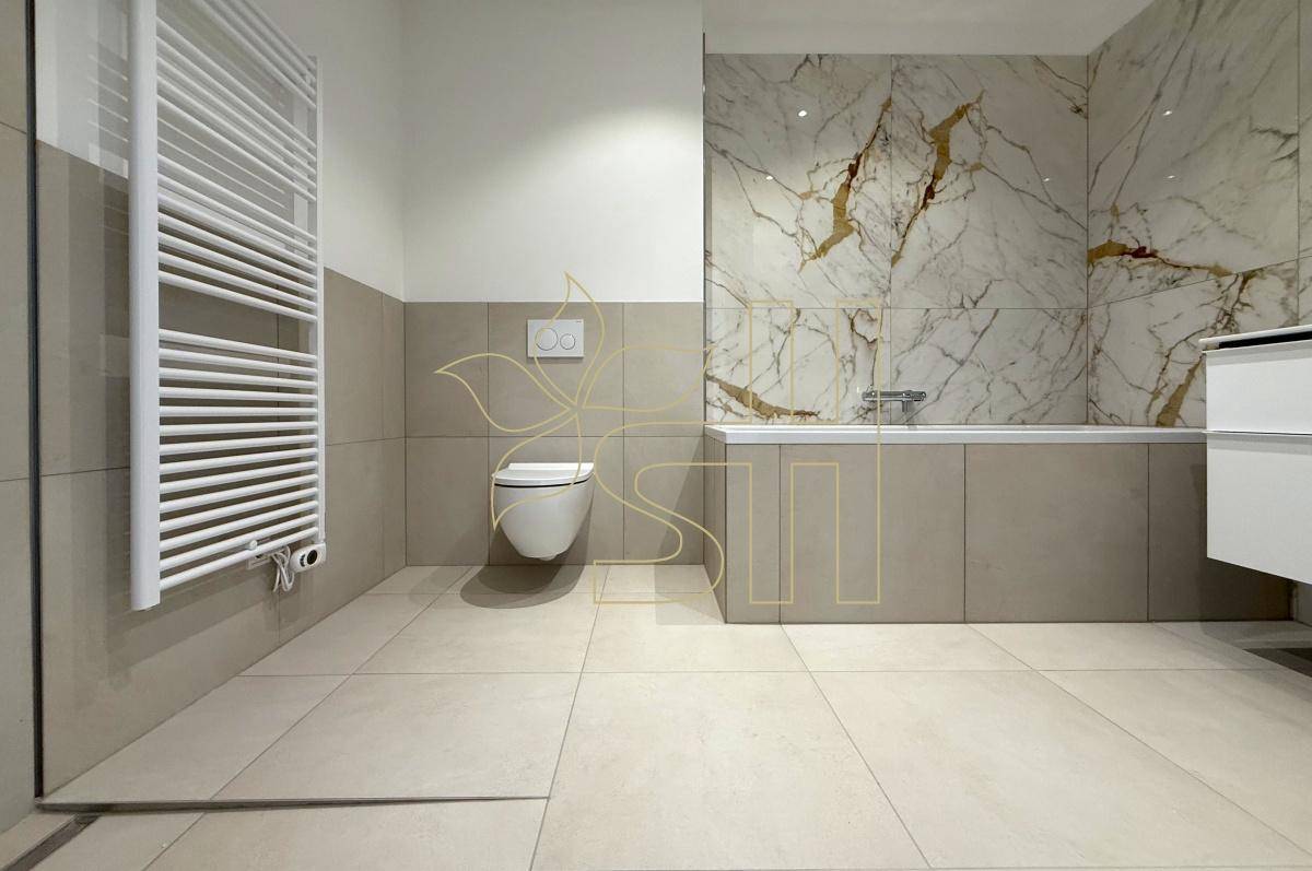Stilvolles Badezimmer mit wandhängendem WC, Badewanne und hochwertigen Fliesen in Beige und Marmoroptik.