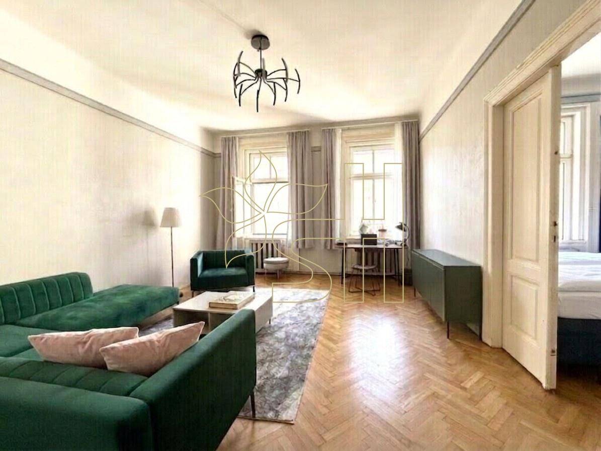 Geräumiges Wohnzimmer mit grünem Sofa, Fischgrätparkett und hohen Fenstern für viel Licht.