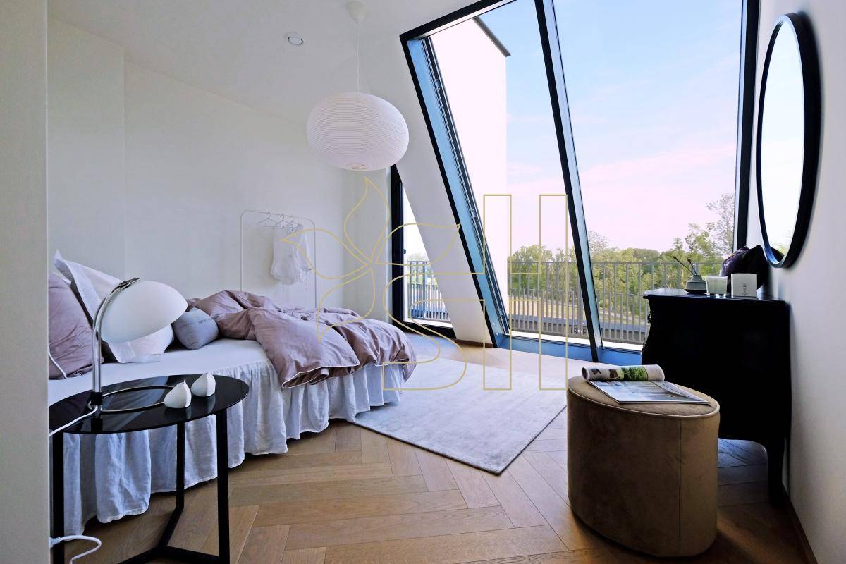 Schlafzimmer mit schrägen Fensterfronten, Holzboden und weitem Blick ins Grüne.