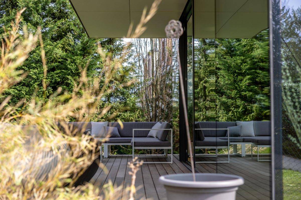 Gemütlicher Außenbereich mit modernen Sitzmöbeln auf einer Holzterrasse, umgeben von viel Grün.
