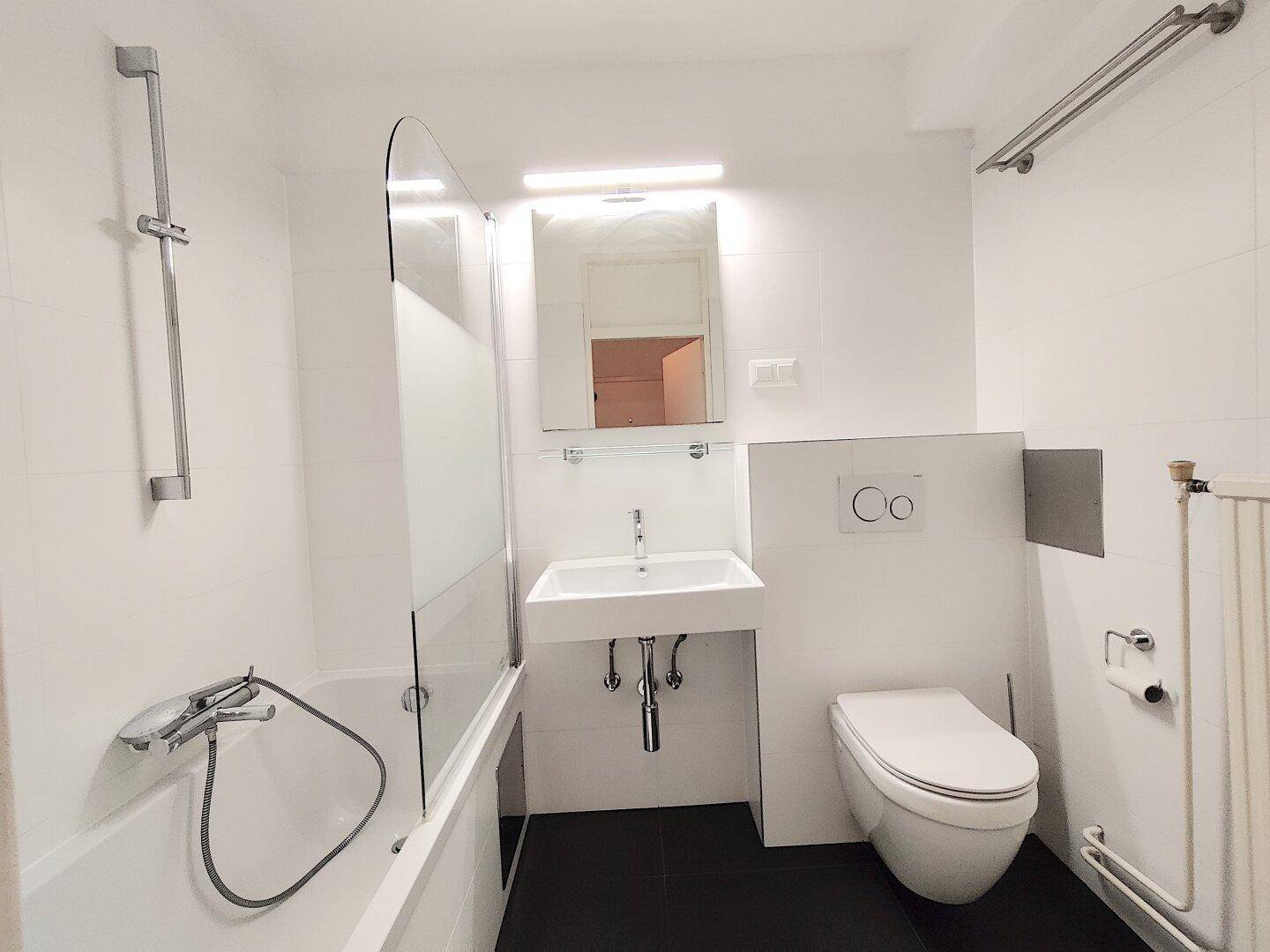 Modernes Badezimmer mit wandhängendem WC, Waschbecken und Badewanne mit Duschfunktion.