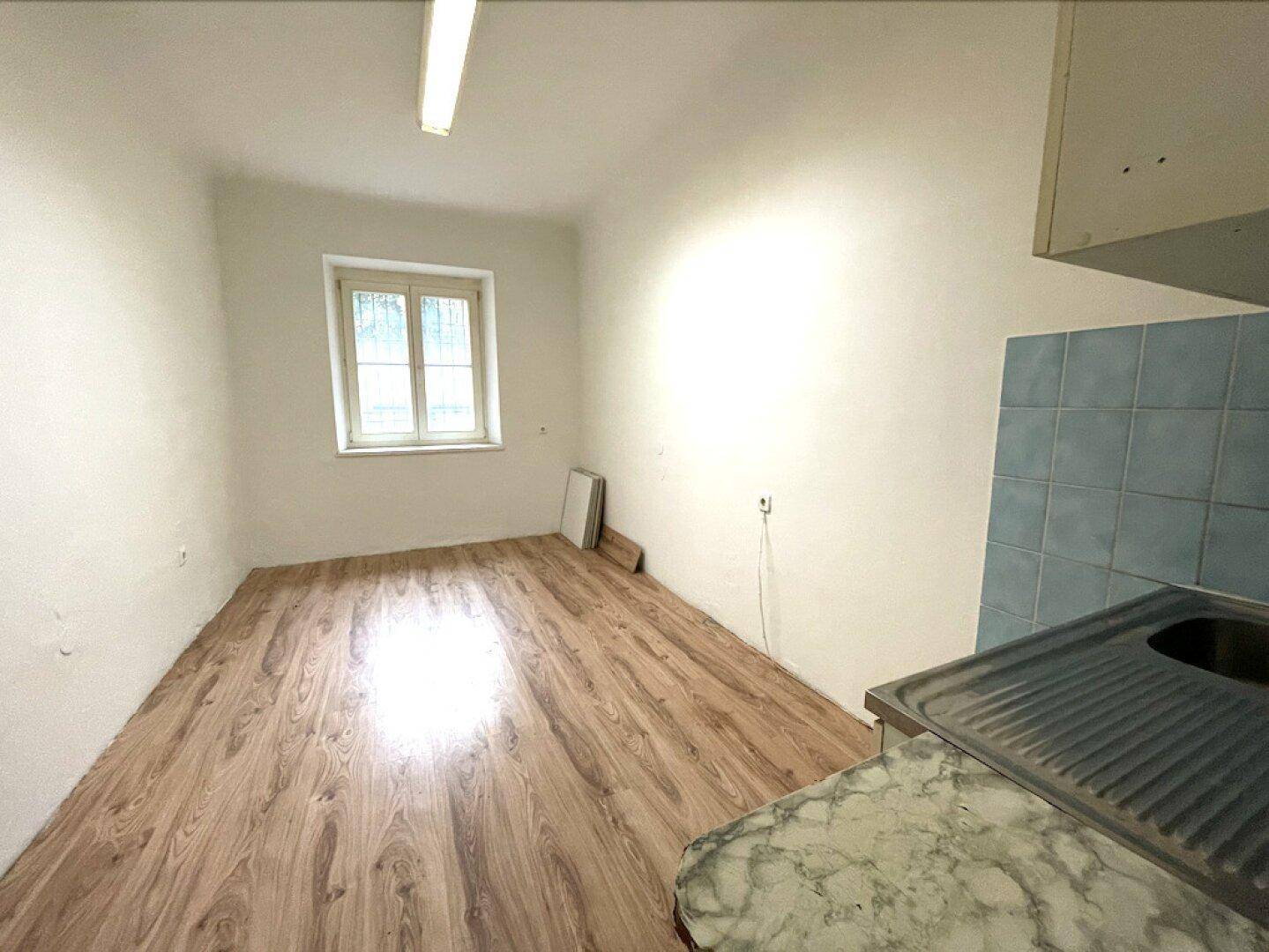 Kleiner Raum mit Fenster, Laminatboden in Holzoptik und einer einfachen Küchenzeile in der Ecke.