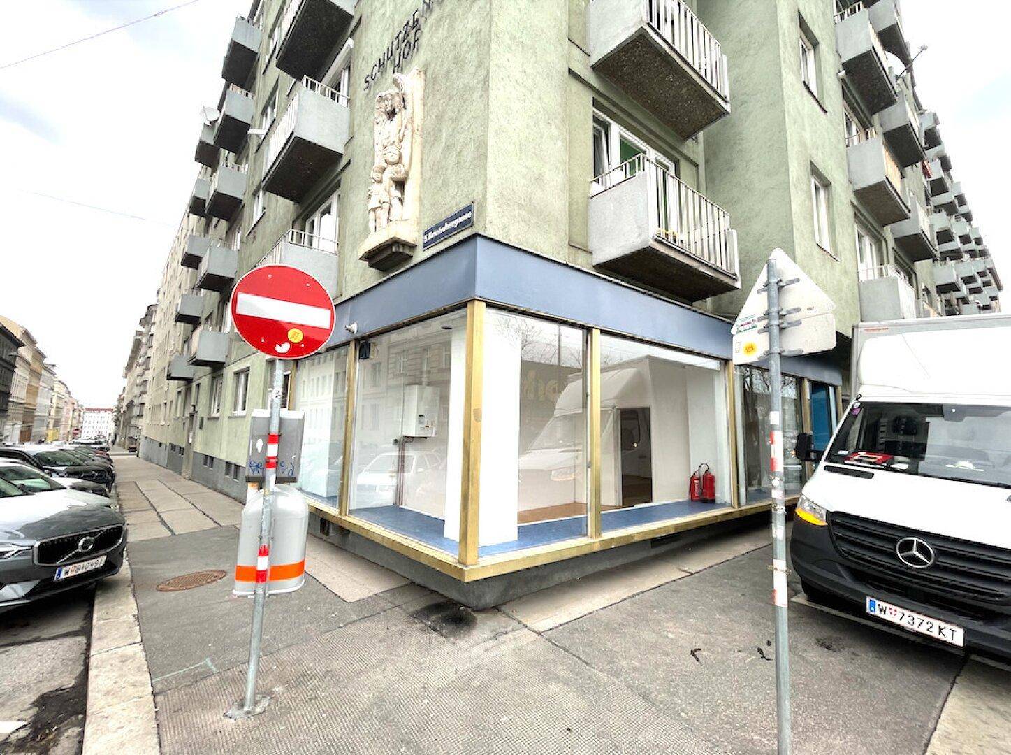 Eckgebäude mit großen Schaufenstern eines leeren Ladenlokals an einer städtischen Straße.