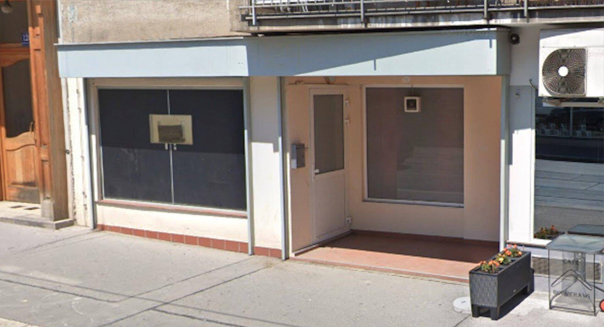 Geschäftsfassade mit einem geschlossenen Rollladen vor einem Fenster und einem Eingang mit Glastür.