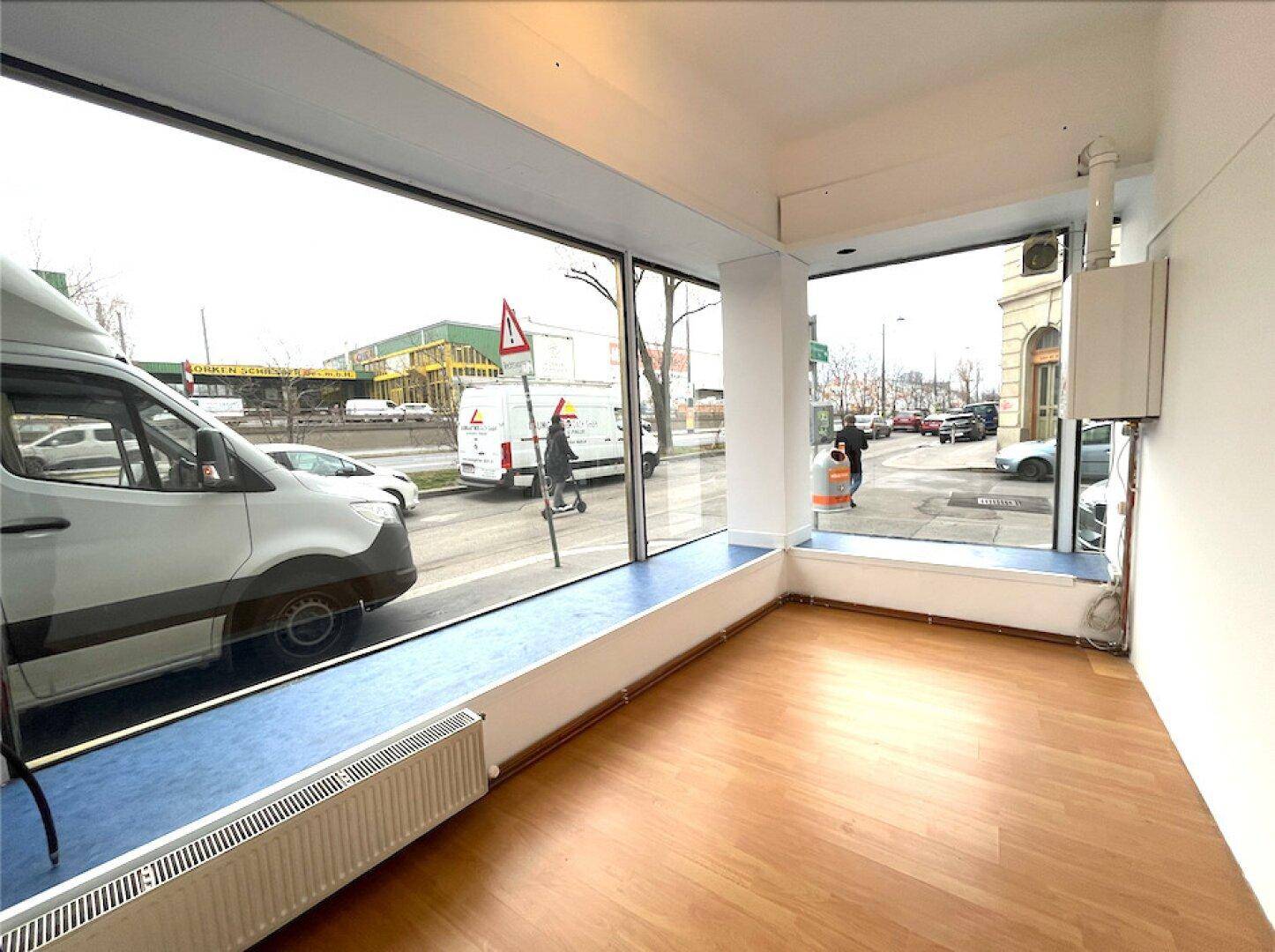 Heller Gewerberaum mit großen Schaufenstern zur Straße und Holzfußboden.