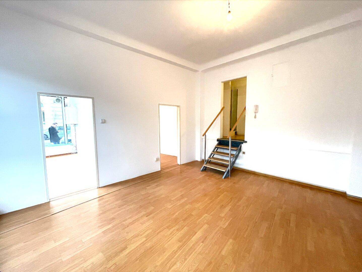 Großer, heller Gewerberaum mit Holzfußboden und Zugang zu weiteren Räumen sowie einer Treppe.