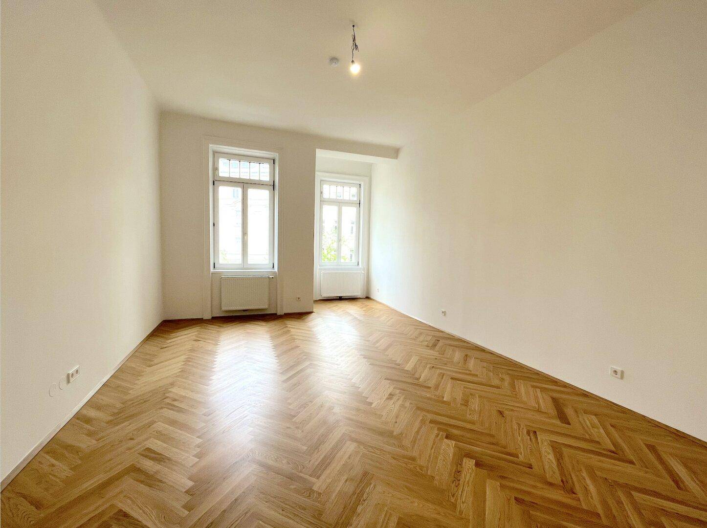 Geräumiges Zimmer mit klassischem Fischgrätparkett und zwei hohen Fenstern, frisch renoviert.