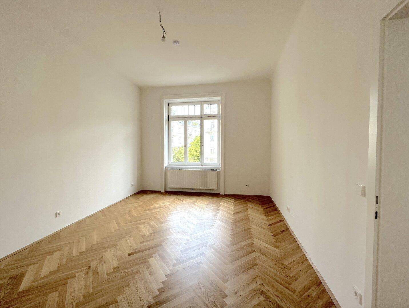 Geräumiges Zimmer mit Fischgrätparkett und einem großen Fenster, das viel Licht spendet.