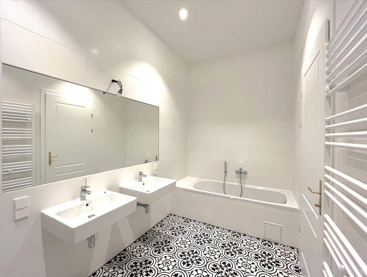 Modernes Badezimmer mit Doppelwaschbecken, Badewanne und gemusterten Bodenfliesen in Schwarz-Weiß.