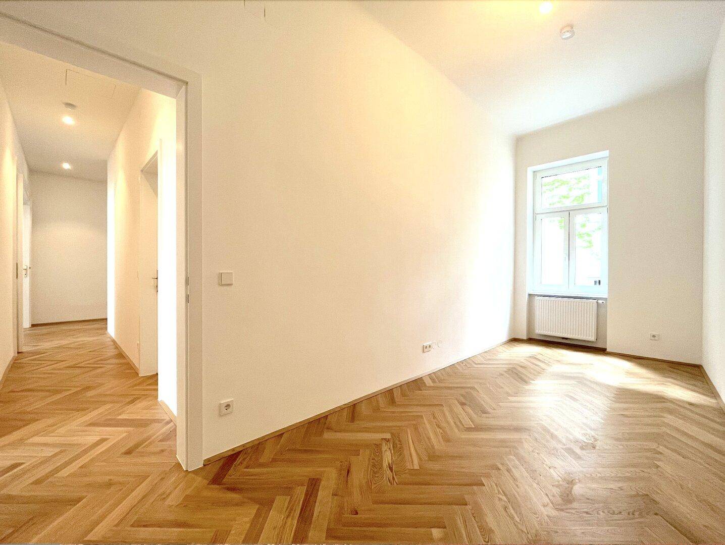 Helles Zimmer mit Fischgrätparkett und einem Fenster, das viel Tageslicht hereinlässt.