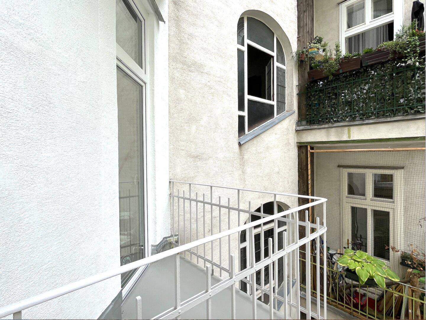 Schmaler Balkon mit weißem Geländer und Blick auf die umliegenden Altbaufassaden im Innenhof.