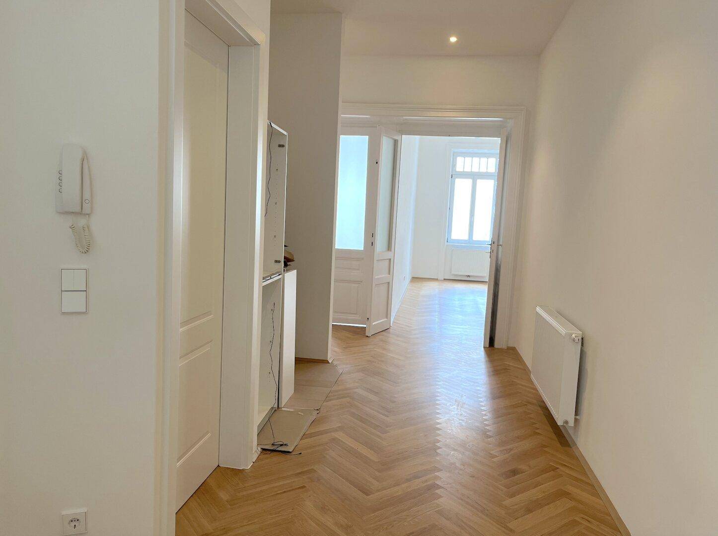 Heller Flur mit Fischgrätparkett, Gegensprechanlage und Zugang zu weiteren Räumen der Wohnung.
