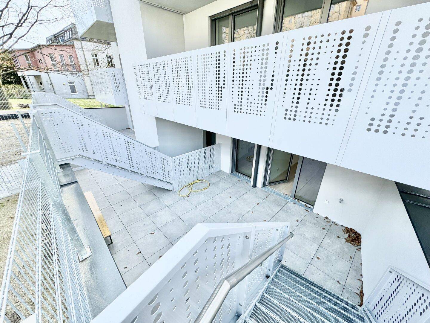 Moderne Terrassenanlage mit perforierten Geländern und Treppen, die verschiedene Ebenen verbinden.