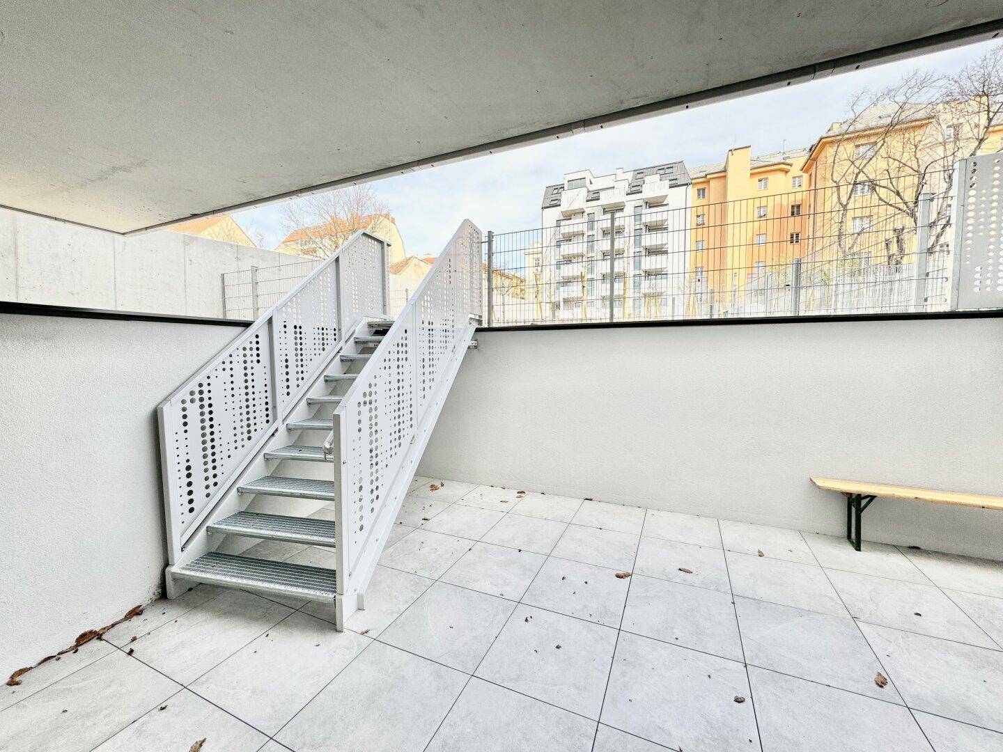 Geräumige Terrasse mit Fliesenboden und moderner Metalltreppe zu einer oberen Ebene.